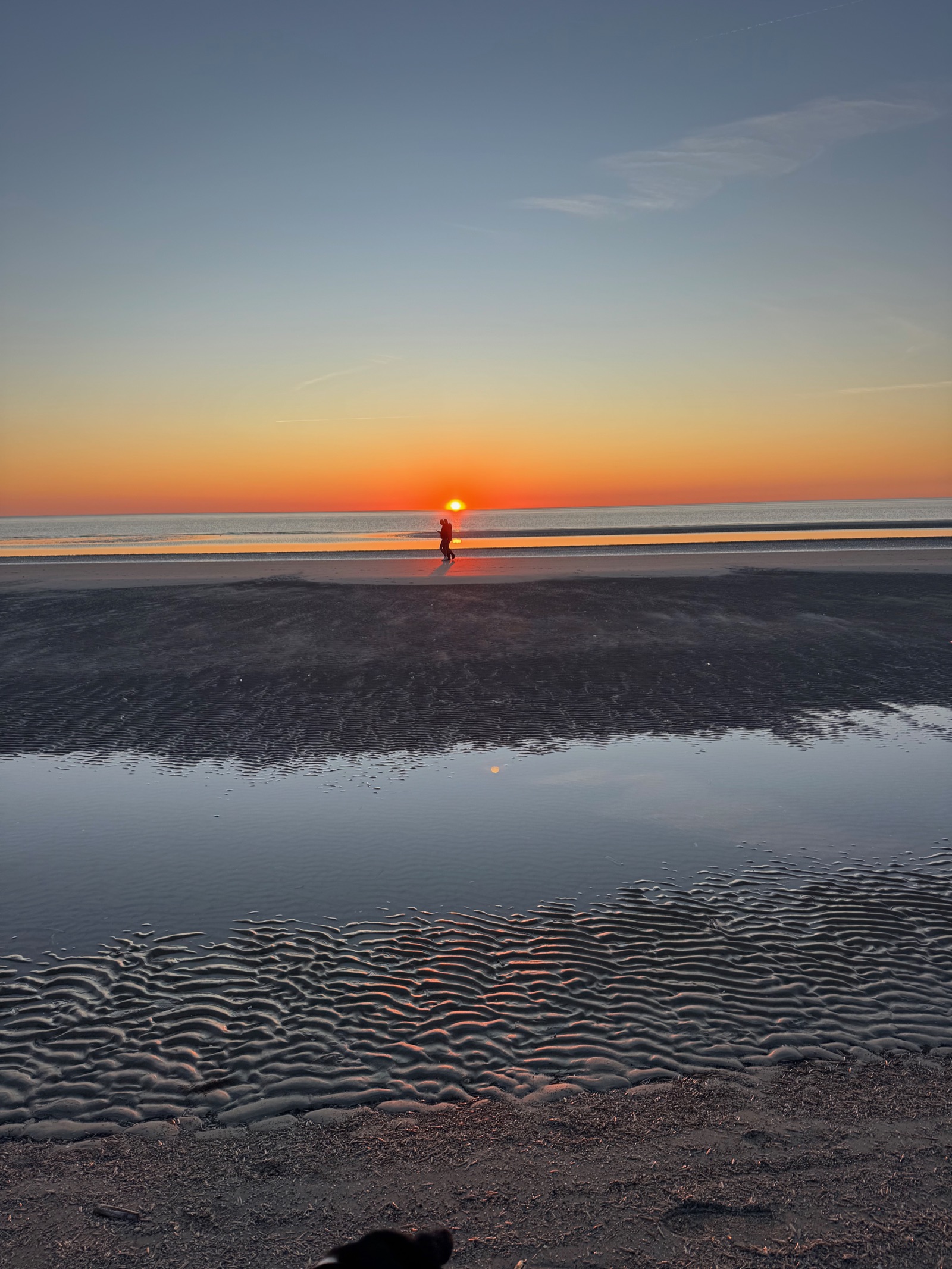 Wattläufer — zwei Menschen als Silhouette auf spiegelnassem Wattsand bei Sonnenuntergang, St. Peter-Ording